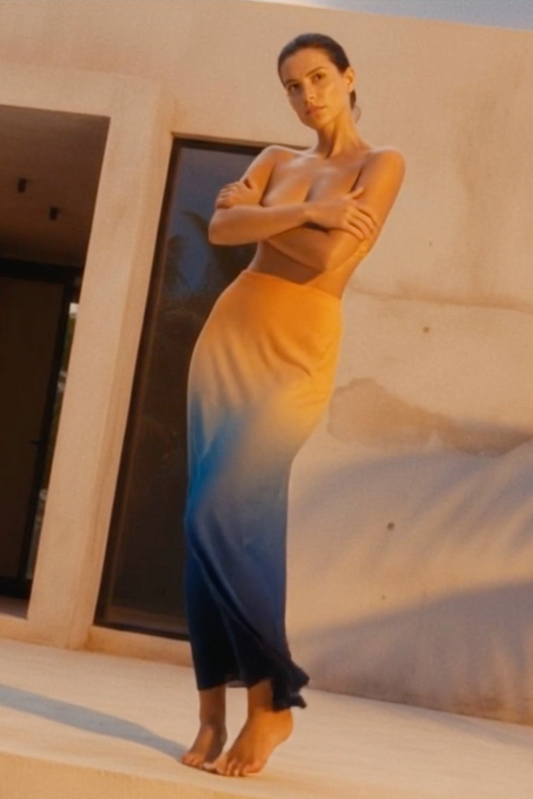 Woman in a long, flowing dress standing in front of a beige wall.