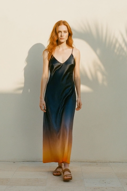 Woman wearing a gradient dress standing against a light wall with palm leaf shadows.