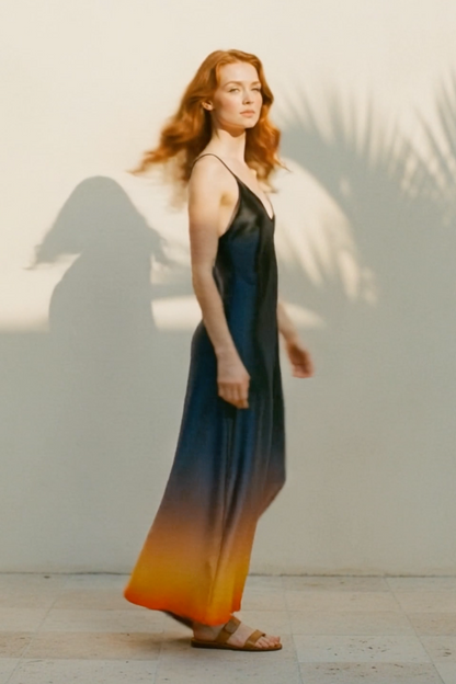 Woman wearing a long, gradient dress with blue, orange, and red colors against a neutral background.