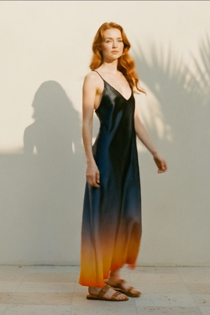 Woman wearing a gradient dress standing against a light background with palm tree shadows.