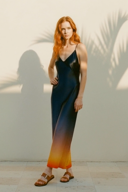 Woman in a gradient dress standing against a light wall with palm leaf shadows.