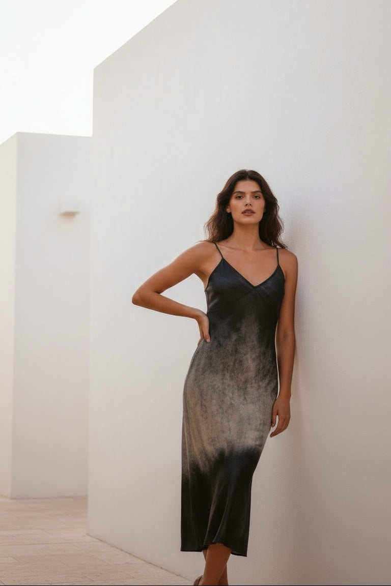 Woman wearing a black and gray gradient dress against a white wall.