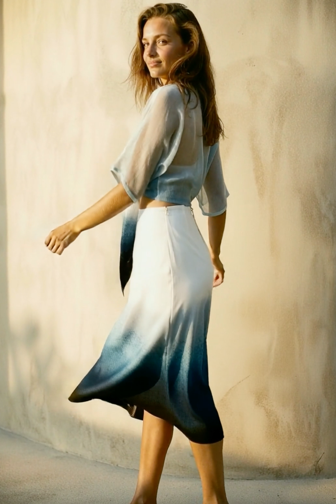 Woman wearing a gradient dress standing against a neutral wall.