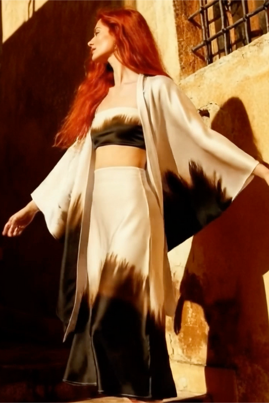 Woman with red hair wearing a white kimono-style outfit against a warm-toned wall.