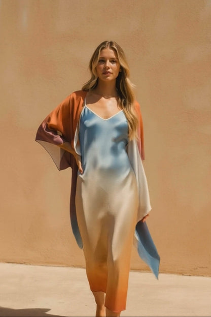 Woman wearing a light blue top and beige skirt with an orange cardigan against a beige wall.