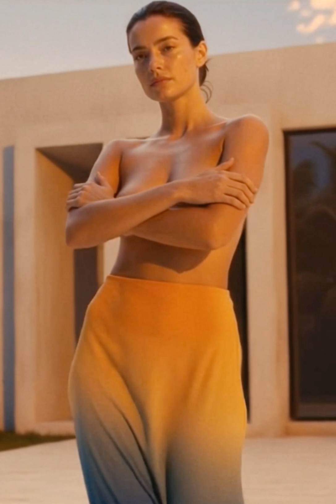 Woman standing with arms crossed wearing a yellow dress in an outdoor setting.