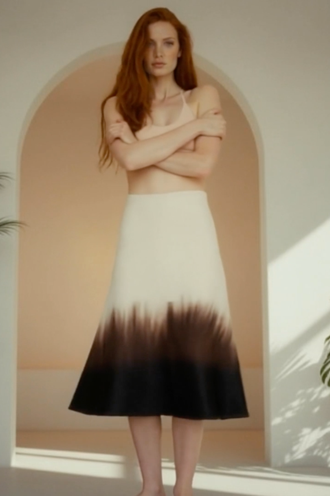 Woman wearing a black and white gradient dress standing in a sunlit room with plants.