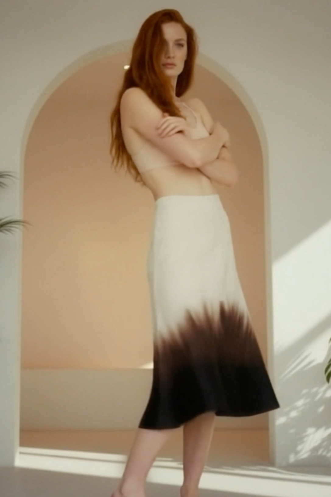 Woman wearing a gradient skirt standing in a sunlit room with plants.