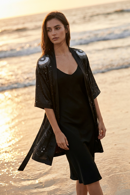 Woman in black outfit standing on a beach with sunset lighting