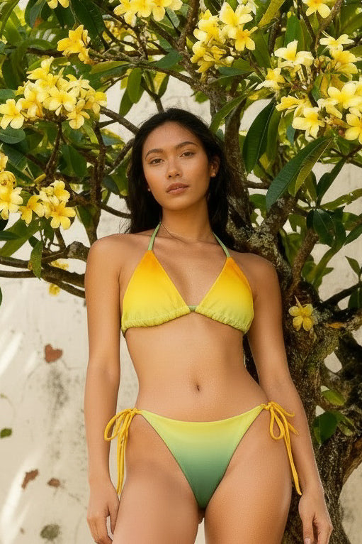 Model wearing a yellow-to-green ombré string bikini under plumeria flowers, sustainable recycled swimwear, Holding Court Horizons collection.