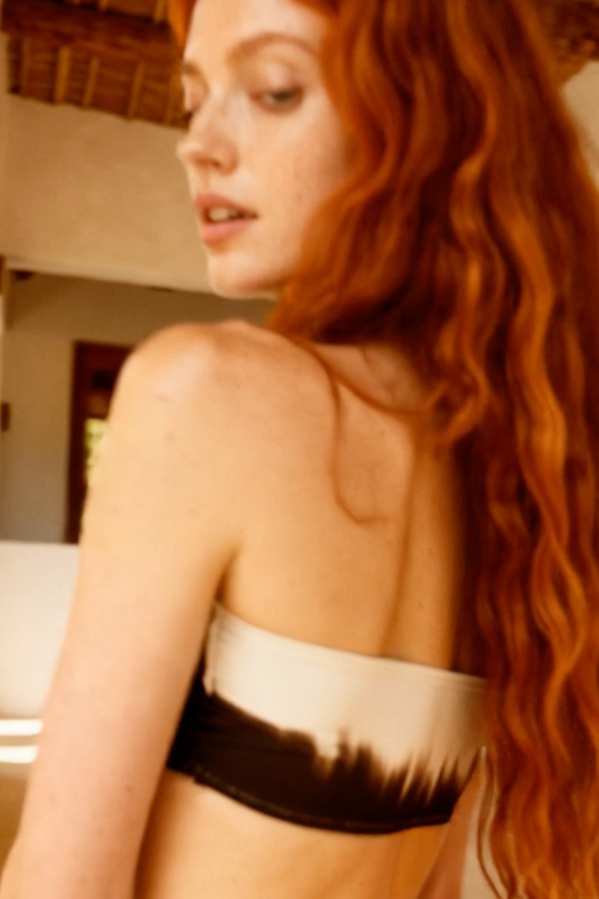Woman with red hair wearing a black and white bikini top in an outdoor setting.