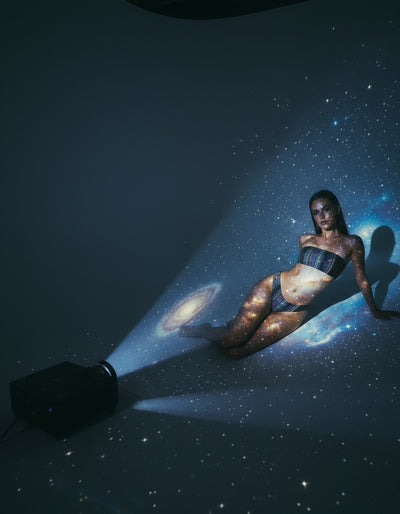 Woman lying on a dark surface with a projector casting a galaxy onto her #Griffin1LunarLanding #MoonArt #SustainableFashion #ArtistsForImpact #BitBasel #LunarArtGallery #ReFiTulum #SpaceArt #EcoFashion #MadeToOrder #OrganicCotton #RecycledFabrics #AuroraBorealis #CosmicFashion #RegenerativeFashion #TheRoyalRobe #CourtneyBarriger #HoldingCourtInc #AstroGLPH #MoonMission2026 #EthicalFashion #SlowFashion #ConsciousClothing #EcoLuxury #SustainableStyle #WatercolorArt #CelestialFashion #FromEarthToMoon #ArtInSpa