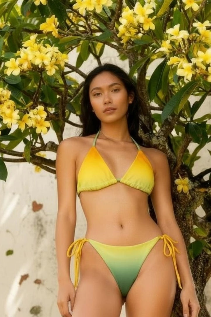 Vega String Bikini in Verde Horizons. Model wearing a yellow-to-green ombré string bikini under plumeria flowers, sustainable recycled swimwear, Holding Court Horizons collection.